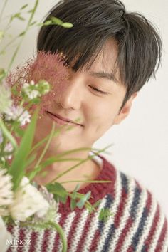 a man holding flowers in front of his face and looking at the camera with eyes closed