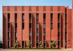 the building is made of red bricks and has many small trees in front of it