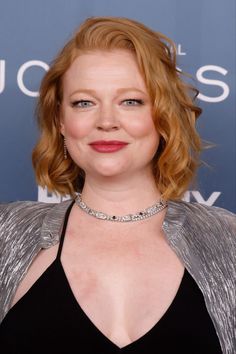 a woman with red hair wearing a black dress and silver jacket smiles at the camera