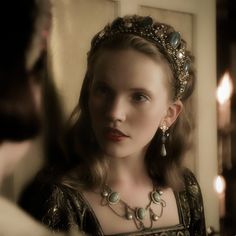 a woman wearing a tiara looking at herself in the mirror with candles behind her