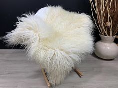 a white chair sitting on top of a wooden floor next to a vase with dry grass in it