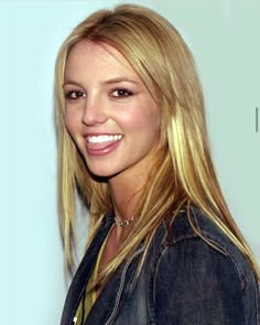 a woman with long blonde hair smiling at the camera and wearing a denim jacket over her shoulders