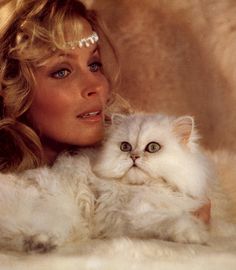 a woman holding a white cat on top of her chest and looking at the camera