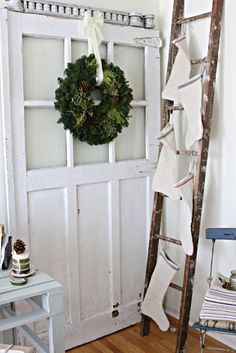 a ladder leaning against a door with a wreath on it and stockings hanging from the top