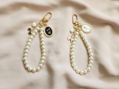 two pairs of earrings with charms on them sitting on a white cloth covered bed sheet