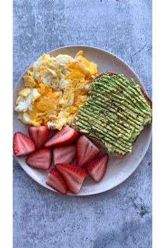 a plate with eggs, avocado and strawberries on it next to toast