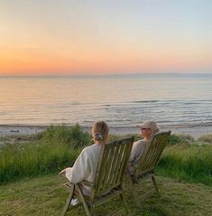 two people sitting on lawn chairs watching the sunset at the beach with their backs to each other