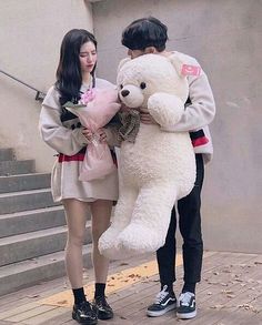 two people standing next to each other holding a large teddy bear