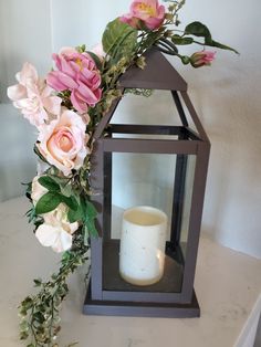 a vase with flowers and a lit candle on a white counter top next to a lantern