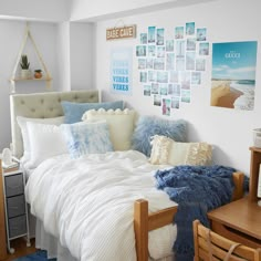 a bed with white sheets and blue pillows in a bedroom next to a wooden table