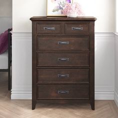 a wooden dresser with drawers in a white room next to a painting on the wall