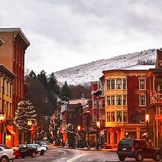 a city street with cars parked on both sides and christmas lights hanging from the buildings