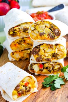 several burritos on a cutting board with fresh fruit and vegetables in the background