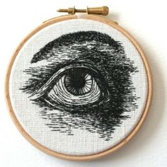 an embroidered eyeball is shown in black and white, on a wooden hoop hanging from the wall