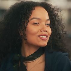 a woman with curly hair wearing a black shirt and green bow tie smiling at the camera