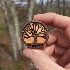 a hand holding a wooden brooch with a tree on it