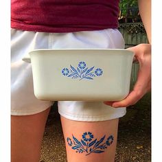 a person holding a white bowl with blue flowers on it's side and the bottom part of their leg