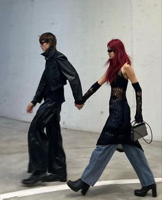 two people dressed in black walking across a parking lot with one holding the other's hand