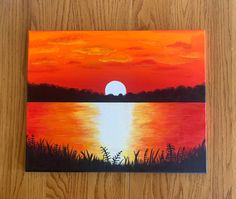 a painting on a wooden surface with the sun setting in the sky and water behind it