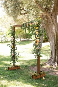 an outdoor ceremony setup with flowers and greenery on wooden poles in front of a tree