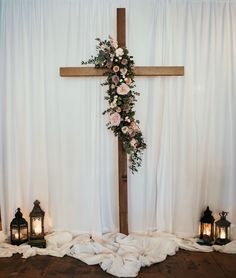 a cross decorated with flowers and candles on a wooden floor in front of white drapes