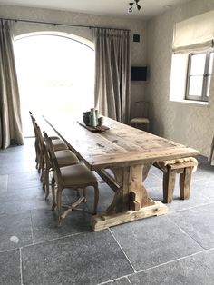 a wooden table sitting in front of a window next to a pair of chairs on top of a stone floor