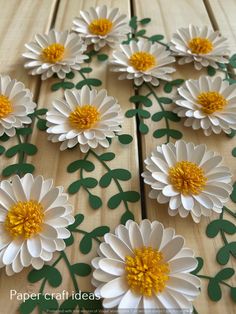 paper flowers are laid out on a wooden table with green leaves and yellow center petals