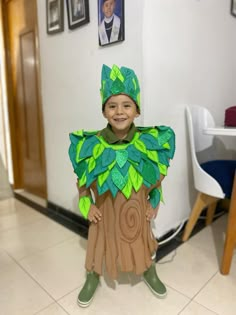 a young boy dressed up as a tree stump with green leaves on his head and shoulders