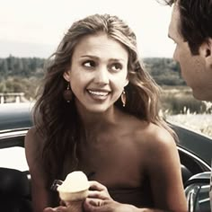 a woman eating an ice cream sundae next to a man in a convertible car