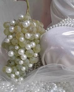 a bunch of grapes and pearls on a white cloth with a bride's dress in the background