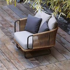 a wicker chair sitting on top of a wooden floor next to a plant and pillows