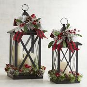 two christmas lanterns decorated with holly, pine cones and red berries are sitting side by side