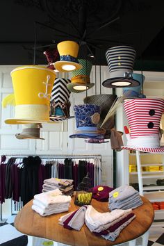 a table topped with lots of different colored hats hanging from it's ceiling next to clothes