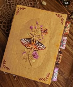 an embroidered book with butterflies and flowers on the cover is sitting on a wooden table