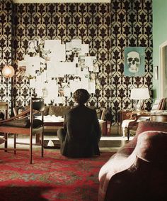 a woman sitting on the floor in front of a living room wallpapered with skulls