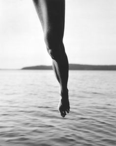 a person jumping into the water from a boat in black and white photo, with their feet dangling over the water