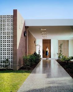 a woman is standing in the doorway of a modern house with green grass and shrubs