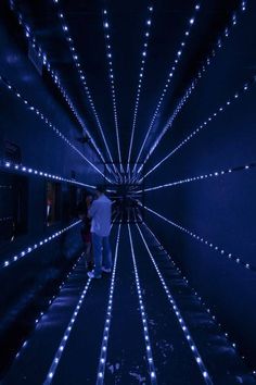 two people walking through a tunnel with blue lights on the walls and floor in front of them