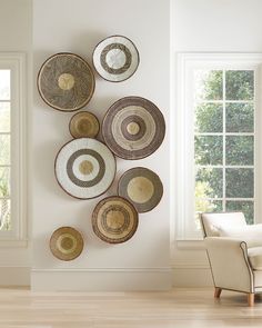 several woven baskets hanging on the wall above a chair in a white room with windows