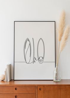 an art print is displayed on a dresser next to a vase with dry grass in it