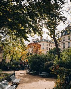 an empty park with benches and trees in the foreground, surrounded by buildings on either side