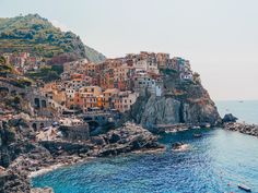 boats are in the water near a small village on a rocky cliff above the ocean