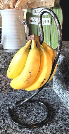 three bananas are hanging from a metal holder on a granite countertop in front of a kitchen sink