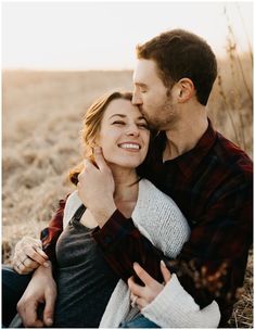 a man and woman cuddle together in the middle of an open field at sunset