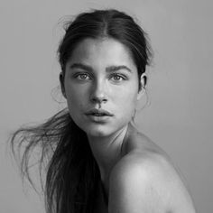 a black and white photo of a woman with her hair blowing in the wind, looking at the camera