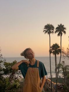 a woman standing on top of a lush green hillside next to the ocean with palm trees