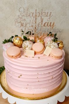 a pink and gold birthday cake with macaroons on top