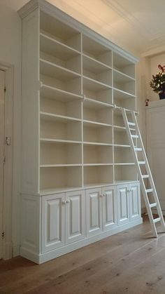 an empty room with white bookcases and a ladder