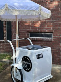 an ice cream cart is parked under an umbrella