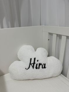 a white cloud shaped pillow with the word hira on it sitting in a crib